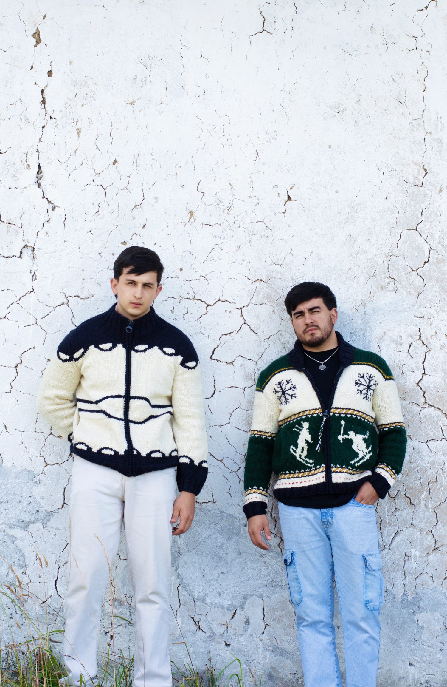 Two people in matching hand-knit sweaters against a whitewashed wall