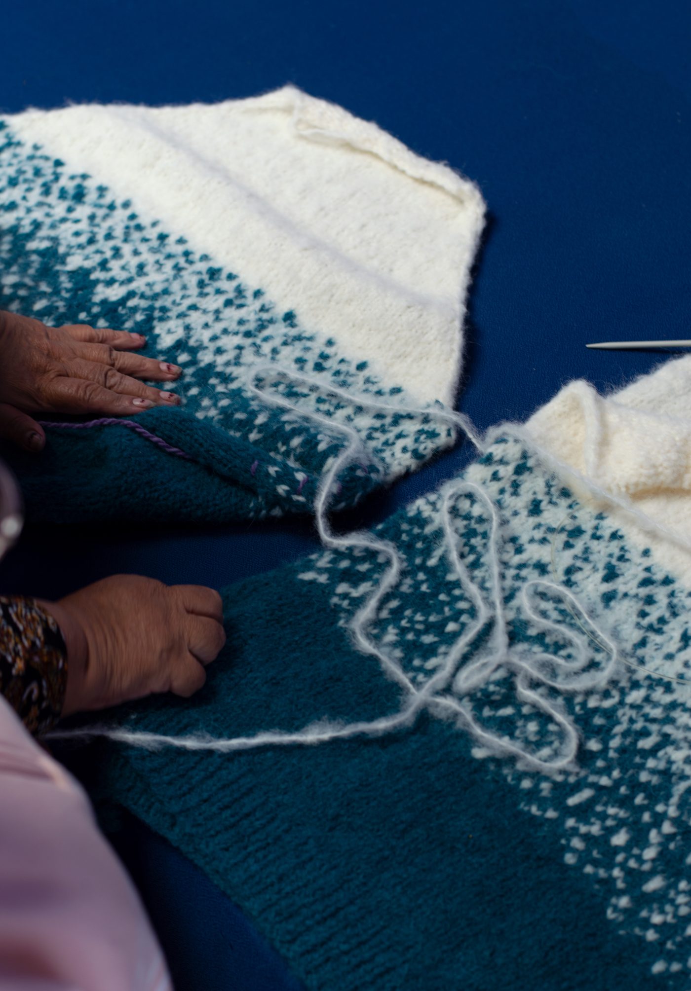 Hands knitting a teal and cream piece